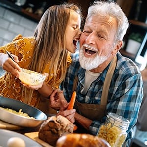 An older man cooks with his granddaughter and shows off his healthier, longer-lasting smile