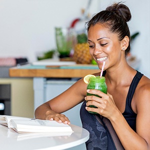 Woman smiling while drinking green smoothie and reading